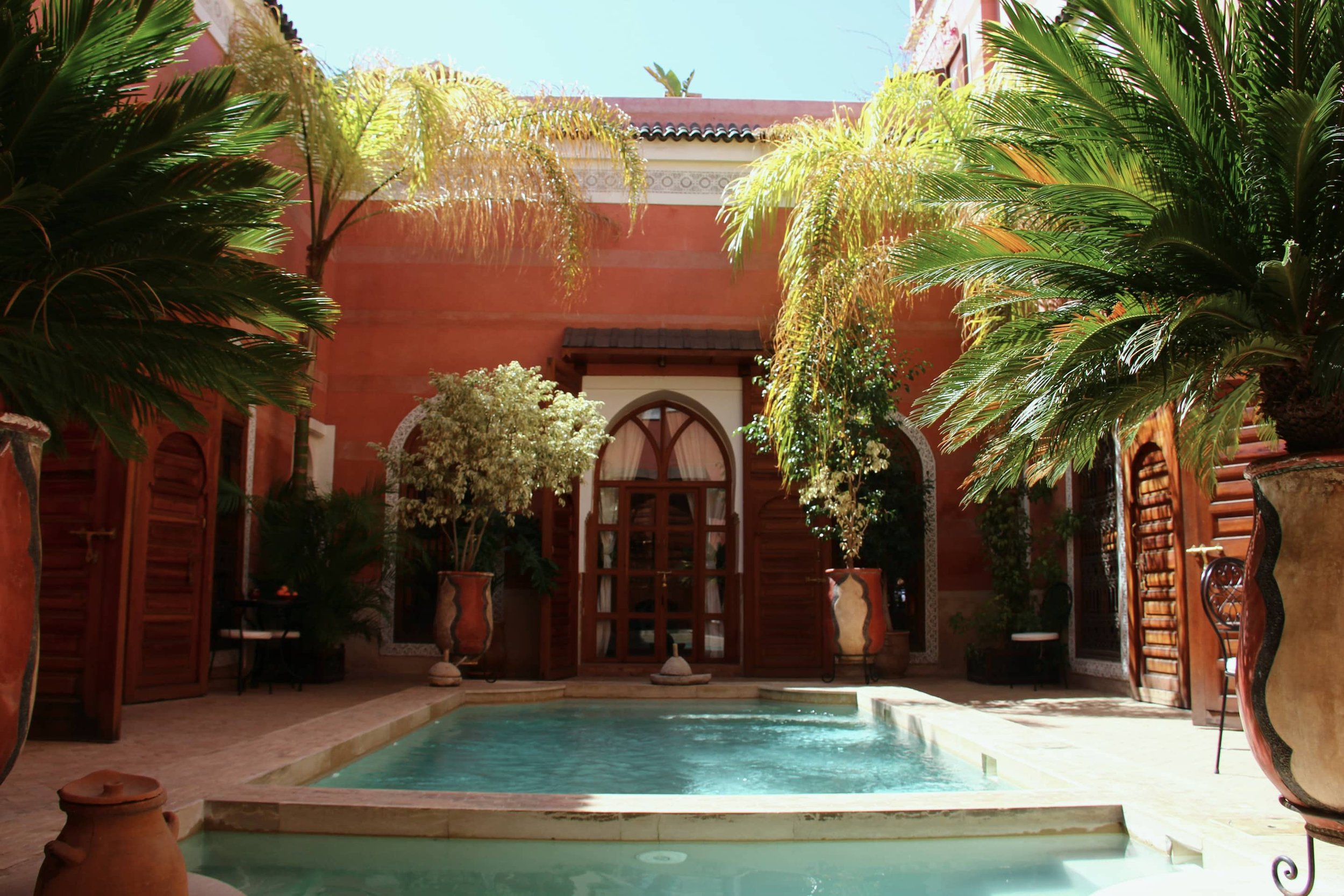 Patio de riad aux murs ocre, bassin et palmiers