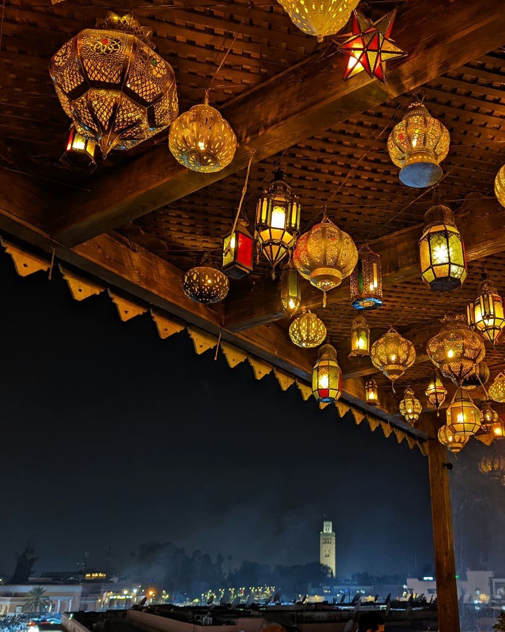Terrasse d’hôtel sur les toits de Marrakech, lanternes allumées face à la Koutoubia