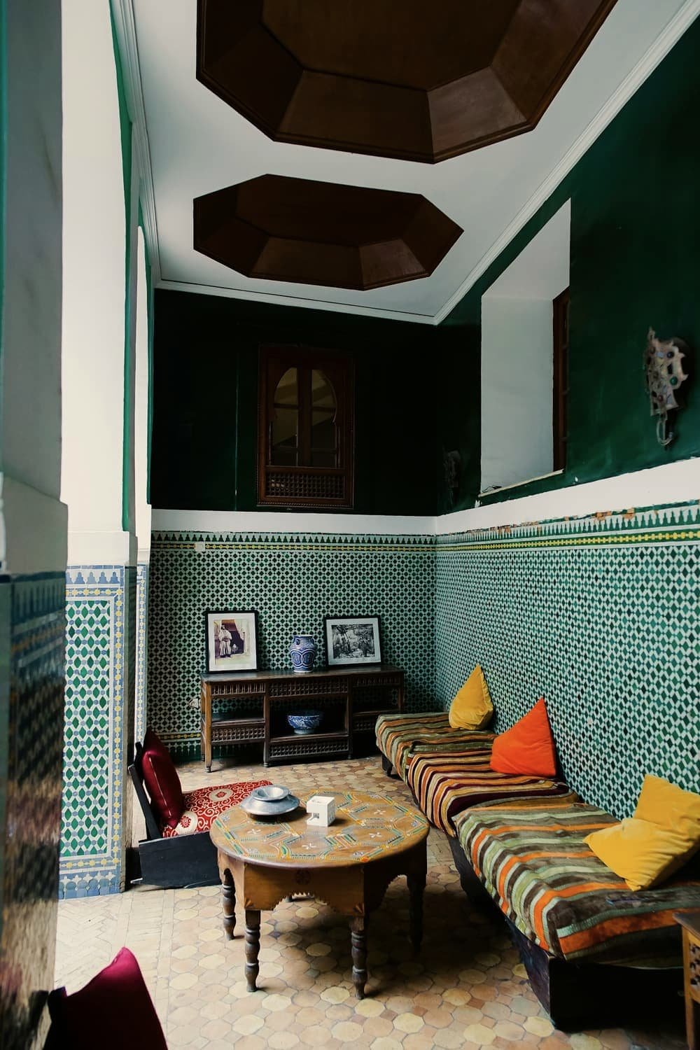 Salon de riad sous un plafond octogonal peint, banquettes et zellige vert