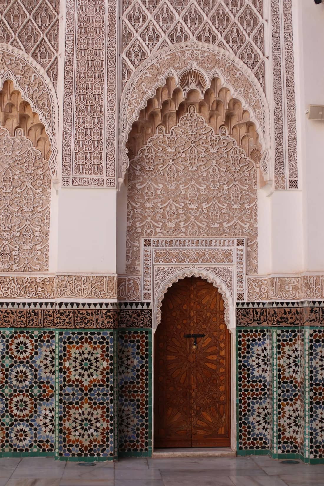 Carved plaster arch opening onto a cedar door and zellige walls