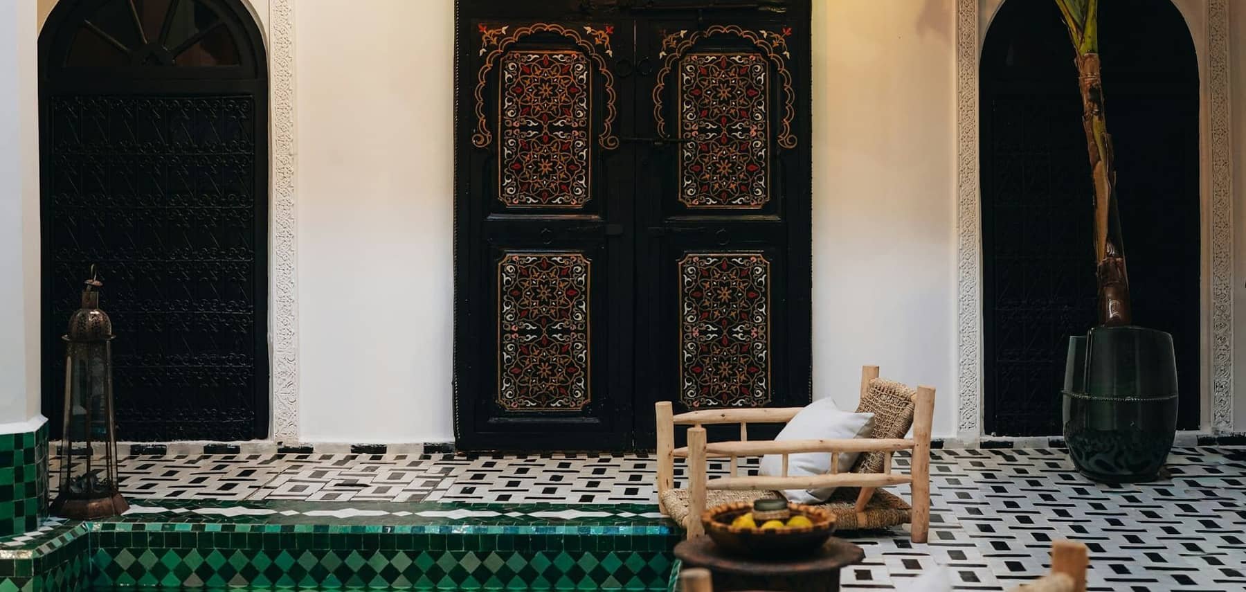 Riad courtyard with painted doors, a chequered floor and a green zellige pool