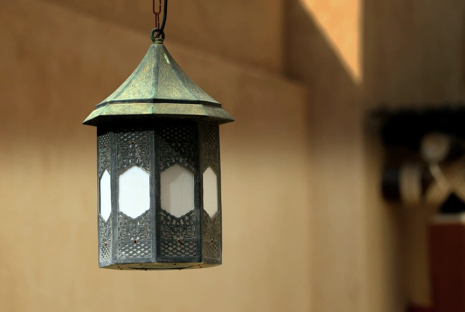 Chased metal lantern hanging in front of a warm-toned wall
