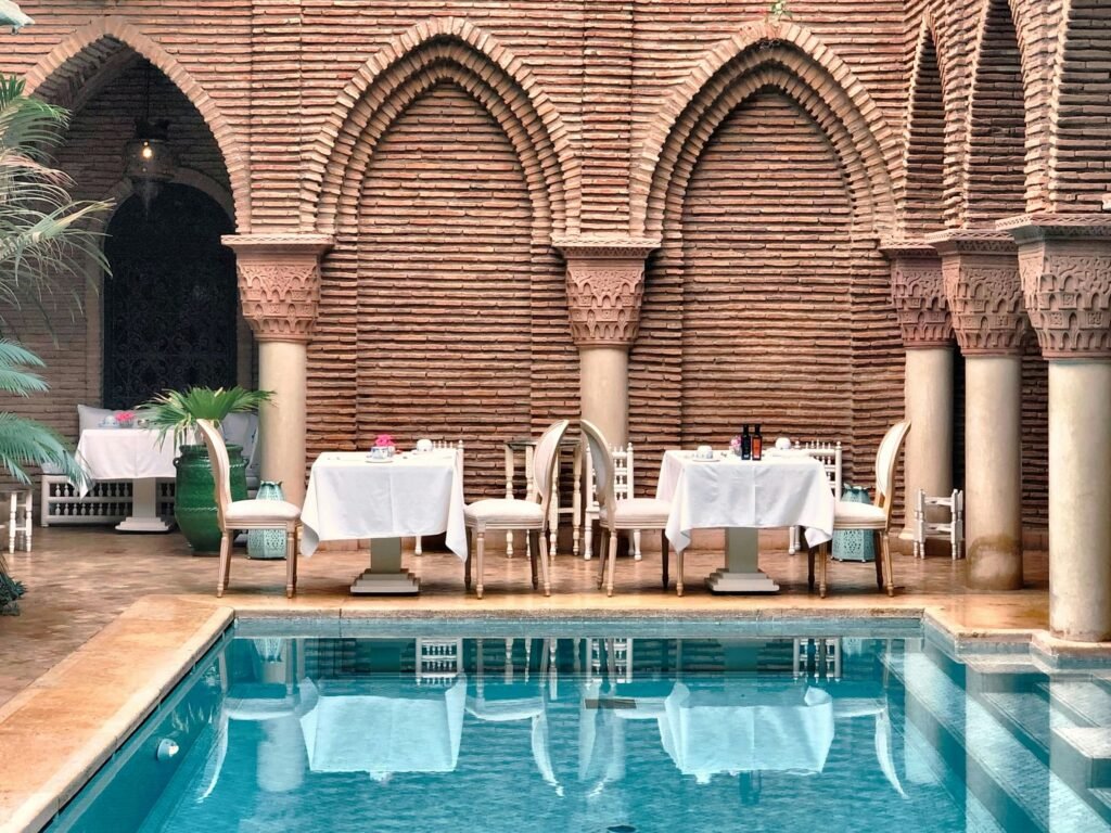 Terrace of a hotel in Marrakech: tables laid by the pool beneath brick arcades