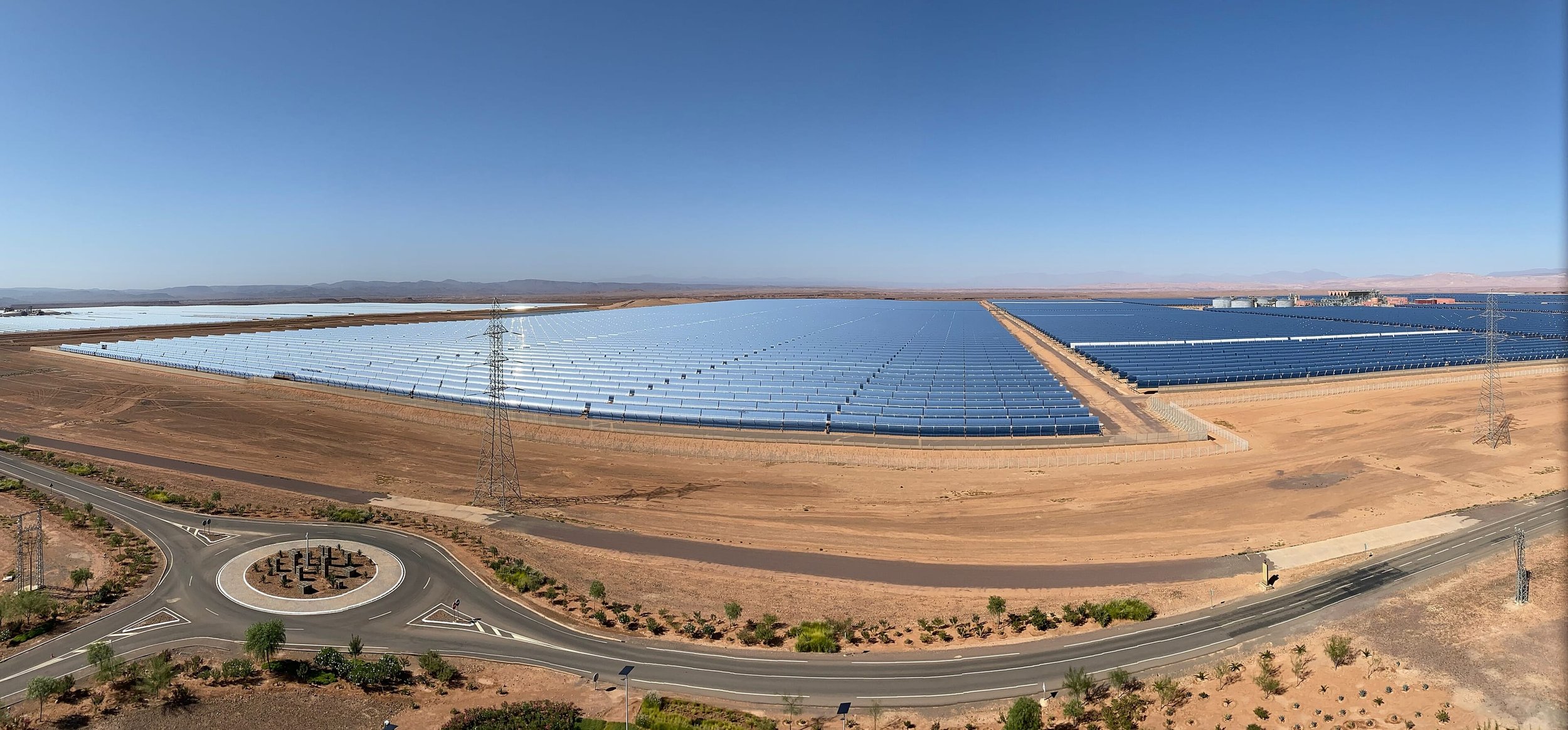 Complexe solaire Noor près d’Ouarzazate : rangées de capteurs solaires dans le désert, rond-point et route d’accès au premier plan